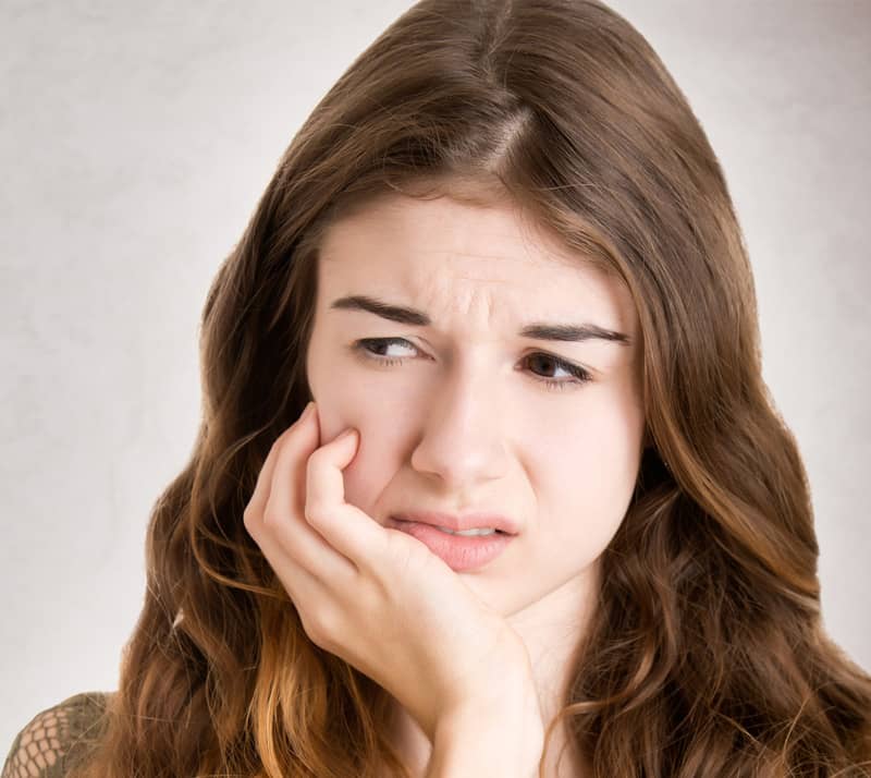 girl holding cheek due to sudden tooth pain